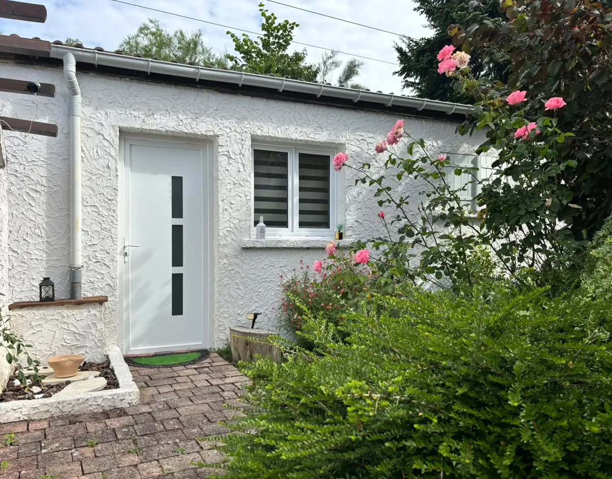 Façade blanche de la maison La promesse de l'Aube entourée de roses et de verdure